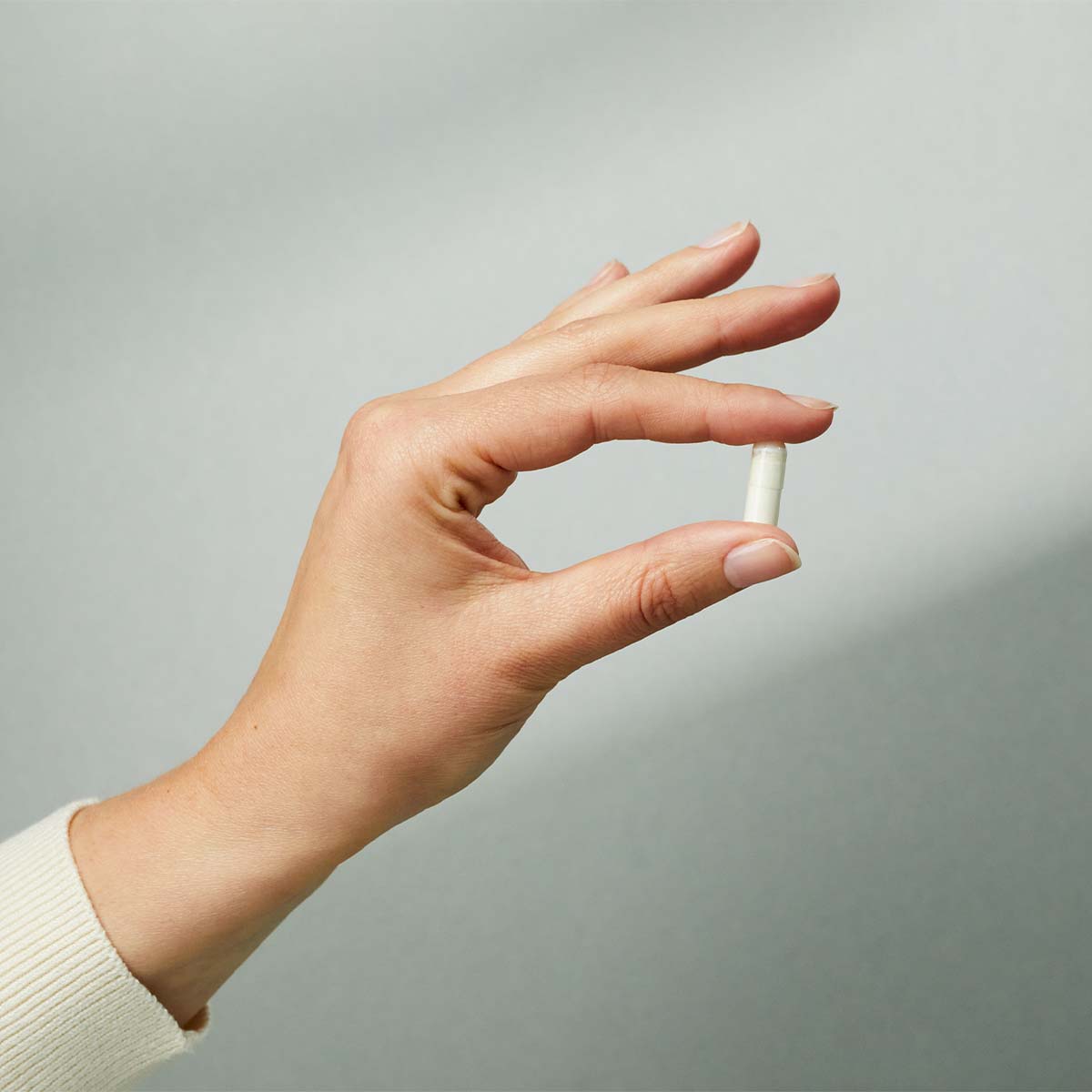 Eine Hand hält eine Kapsel eines Liebscher & Bracht NAahrungsergänzungsmittels zwischen Daumen und Zeigefinger.