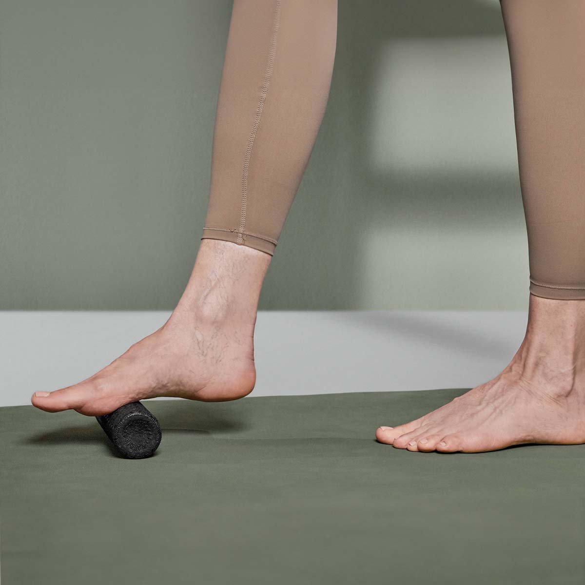 Ein Fuß rollt leicht über eine Mini-Faszienrolle von Liebscher & Bracht, die am Boden liegt. 